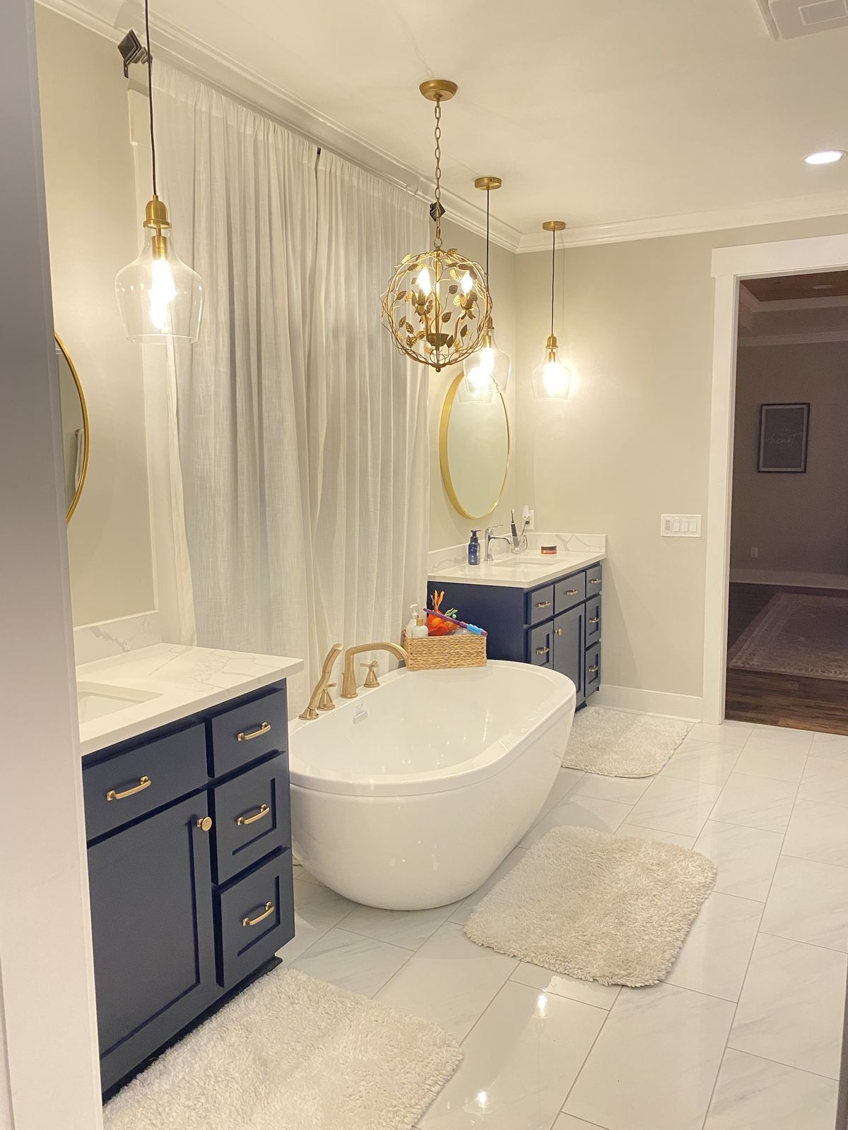Primary bathroom. Navy vanities, quartz tops, brass fixtures, and a freestanding tub.