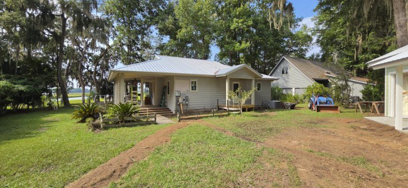 Single-story home. Metal roof, lap siding, and a front porch under moss-draped oaks.