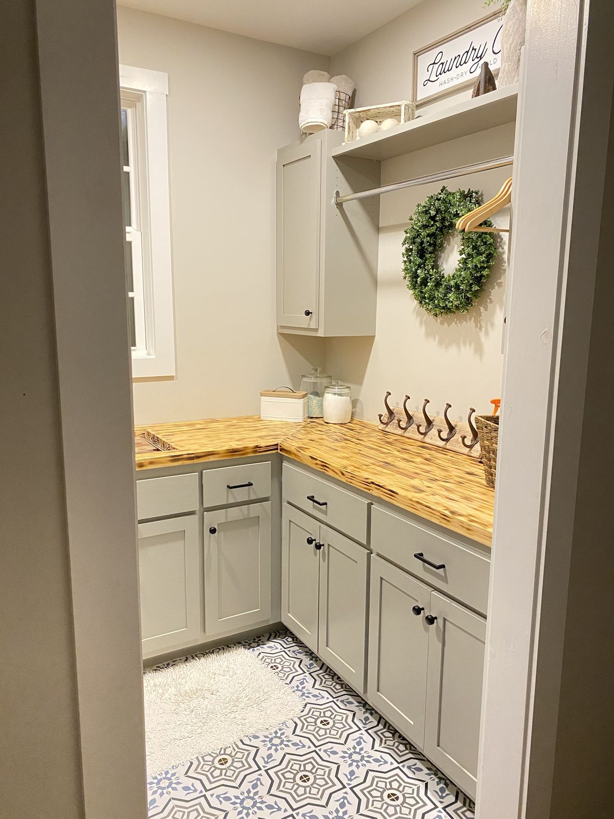Laundry room. Shaker cabinets, wood countertops, hanging rod, and patterned tile floor.
