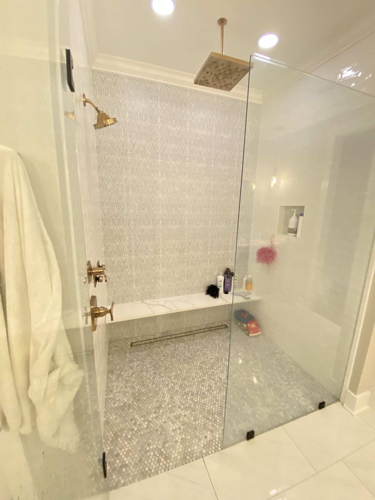 Walk-in shower. Frameless glass, patterned tile wall, quartz bench, and linear drain.