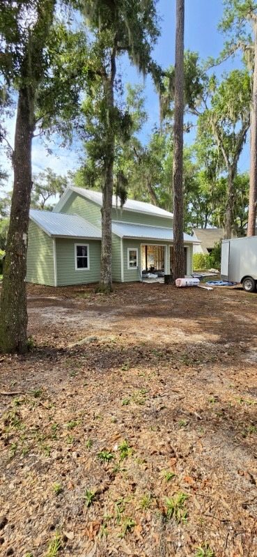 Green two-story home with a metal roof among live oaks